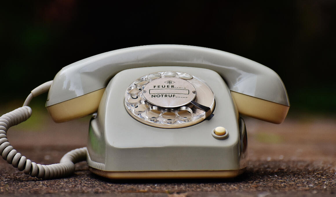 Closeup image of a cream colored rotary phone on the ground outside