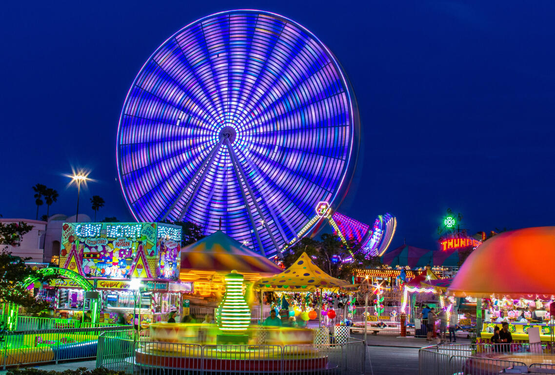 Image of a brightly lit, busy scene at an amusement park with a night sky as the background